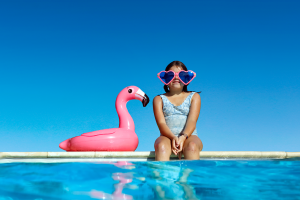 Jeune fille au bord d'une piscine avec des lunettes roses en forme de coeur et une bouée flamant rose